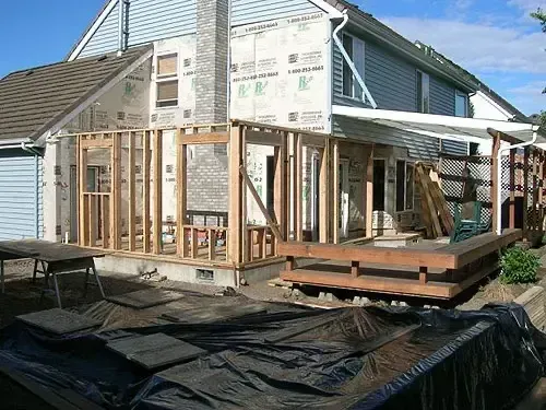 House under renovation with exposed framing and black tarp covering the ground