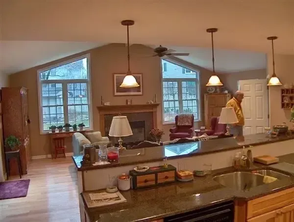 Modern kitchen with island, pendant lights, fireplace, and a person standing near the counter.