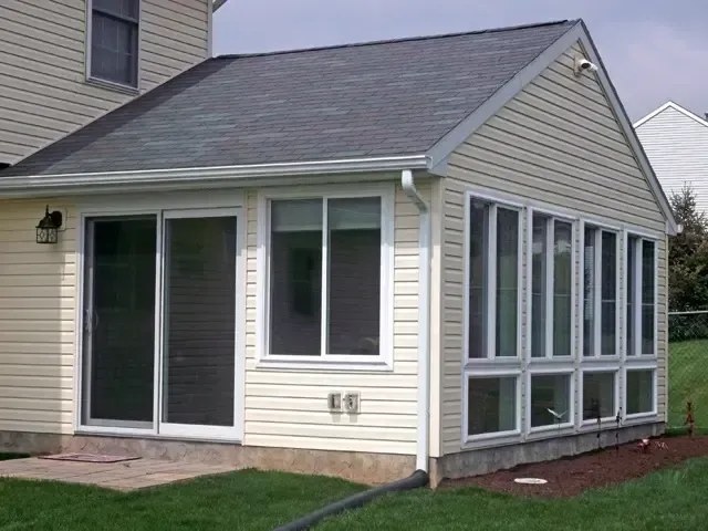 Small beige house with a sliding glass door and a sunroom extension under a gray roof