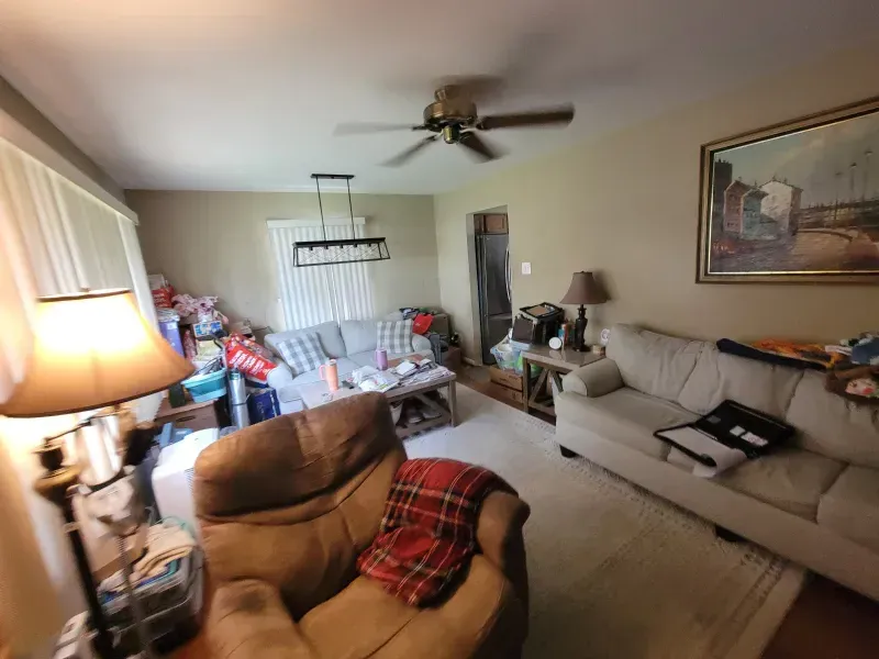 Living room with beige sofas, recliner, ceiling fan, lamp, and holiday decorations near the window