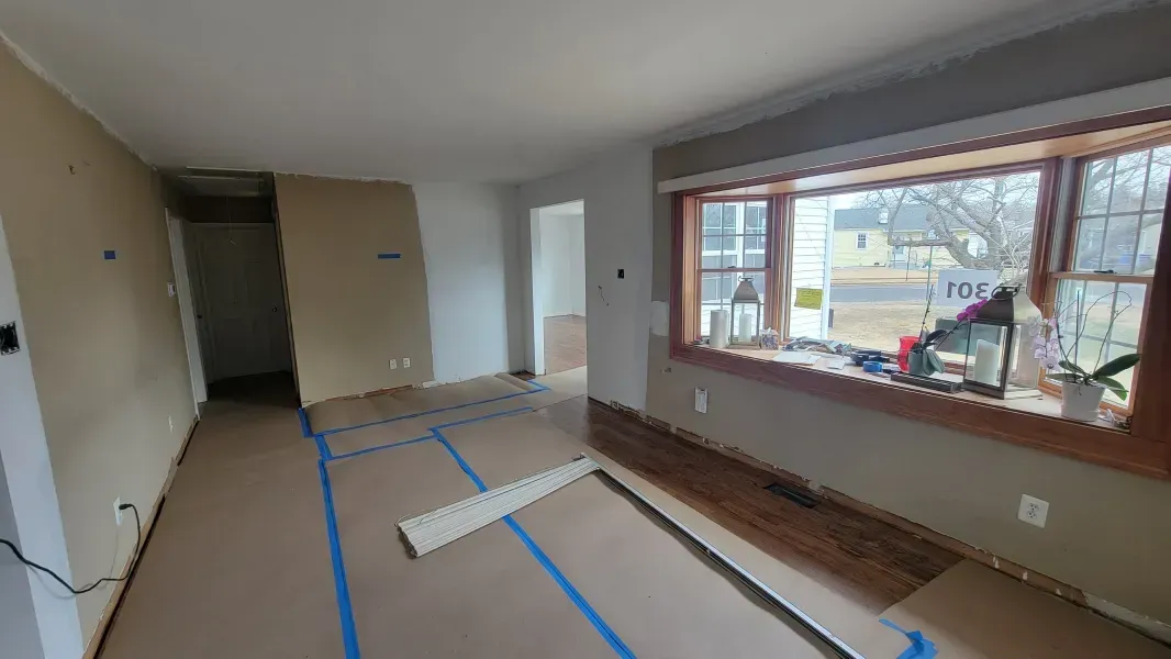 Empty living room under renovation with blue tape on the floor and a large front window
