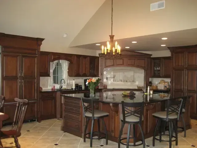 Warm kitchen with dark wood cabinets, island seating, pendant light, and tiled floor