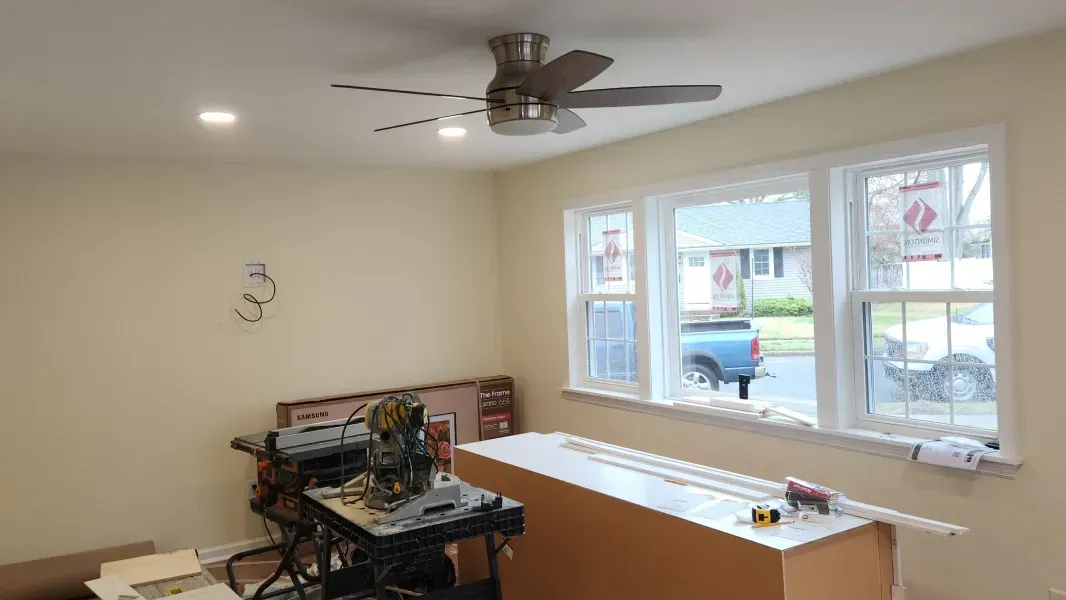 Empty beige living room with ceiling fan, windows, and a cardboard box on a table
