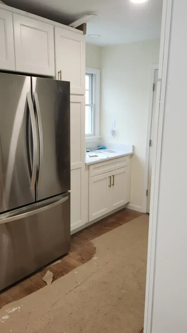 Narrow kitchen with stainless steel refrigerator, white cabinets, and a small window above the sink