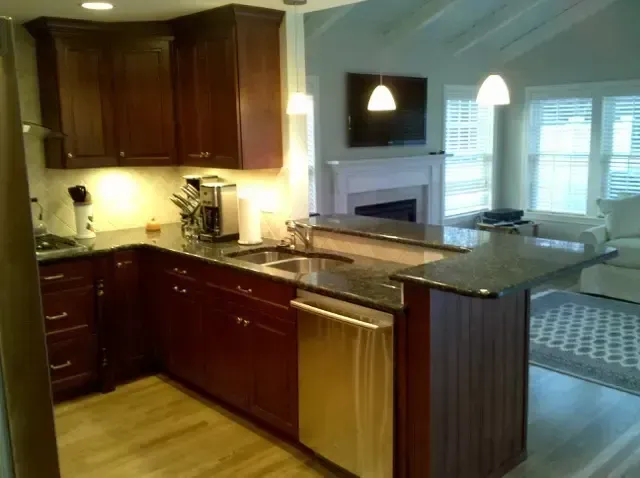 Modern kitchen with dark wood cabinets, granite island, stainless dishwasher, and a breakfast nook by windows