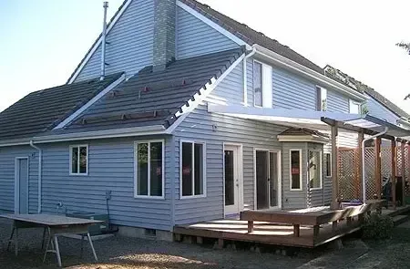 White house with gray siding, large windows, and a wooden deck under construction outdoors