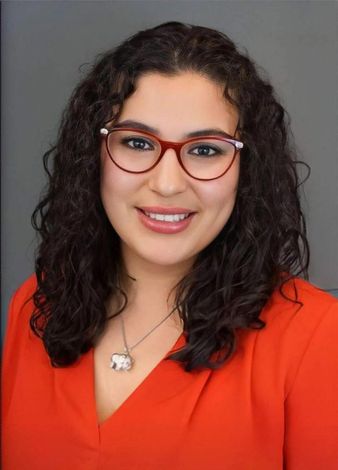 Portrait of a smiling woman with curly hair, red glasses, and a bright red top against a gray background Portrait of a smiling woman with curly hair, red glasses, and a bright red top against a gray background