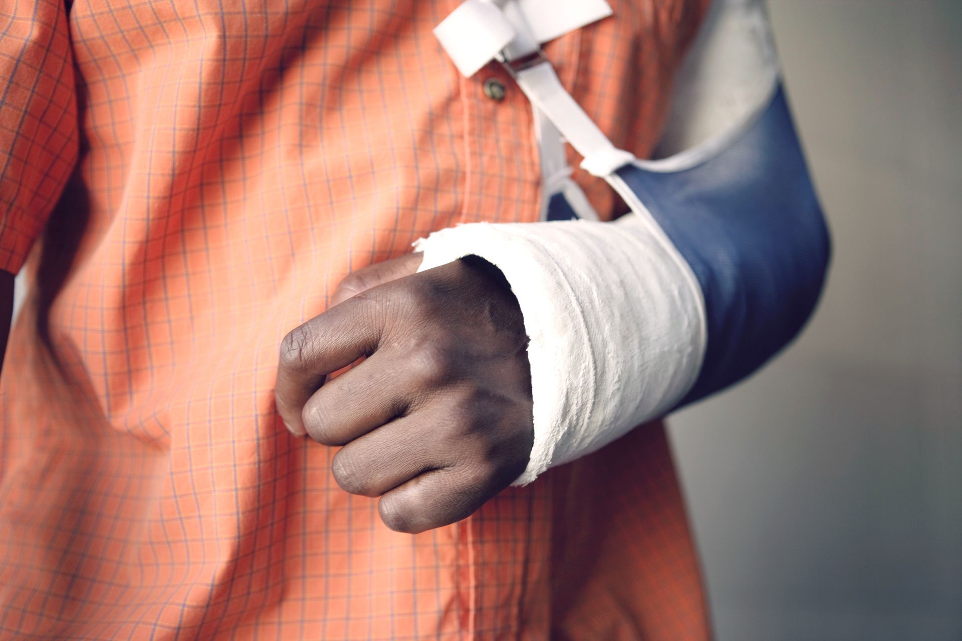 Person with arm in cast, in a sling, wearing orange shirt.