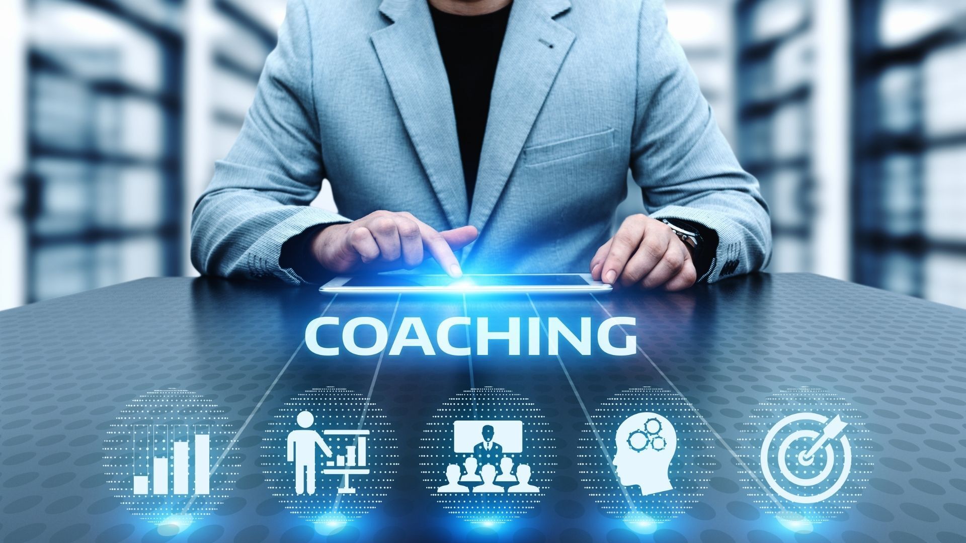 Ein Mann sitzt an einem Tisch und benutzt ein Tablet mit dem Wort „Coaching“ darauf.