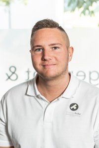 Ein junger Mann in einem weißen Poloshirt lächelt in die Kamera.