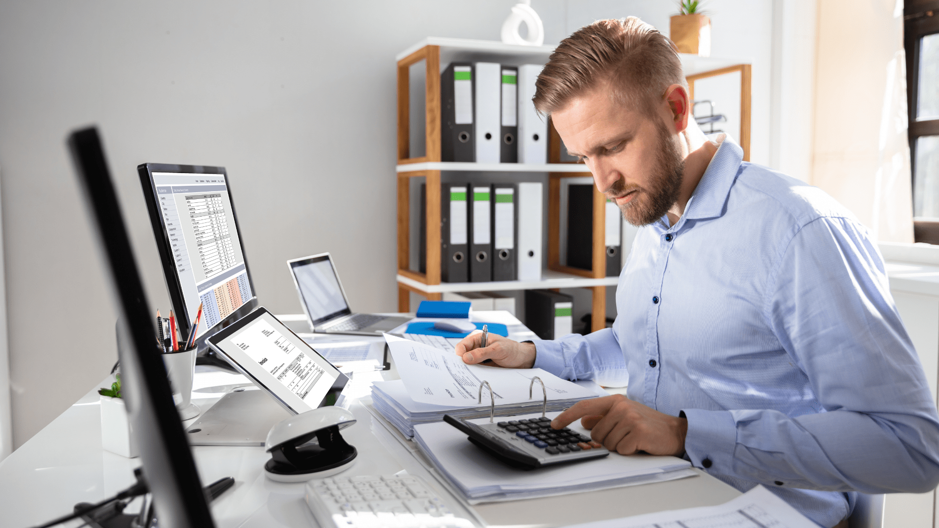 Ein Mann sitzt an einem Schreibtisch vor einem Computer und benutzt einen Taschenrechner.