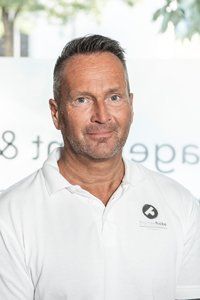 Ein Mann mit Bart trägt ein weißes Hemd und lächelt.