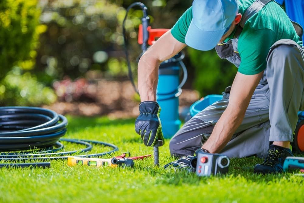 A Man Is Kneeling Down in The Grass Working on A Sprinkler System — Green Vision NT in Virginia, NT