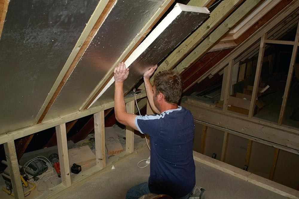 A man is working on a ceiling in an attic.