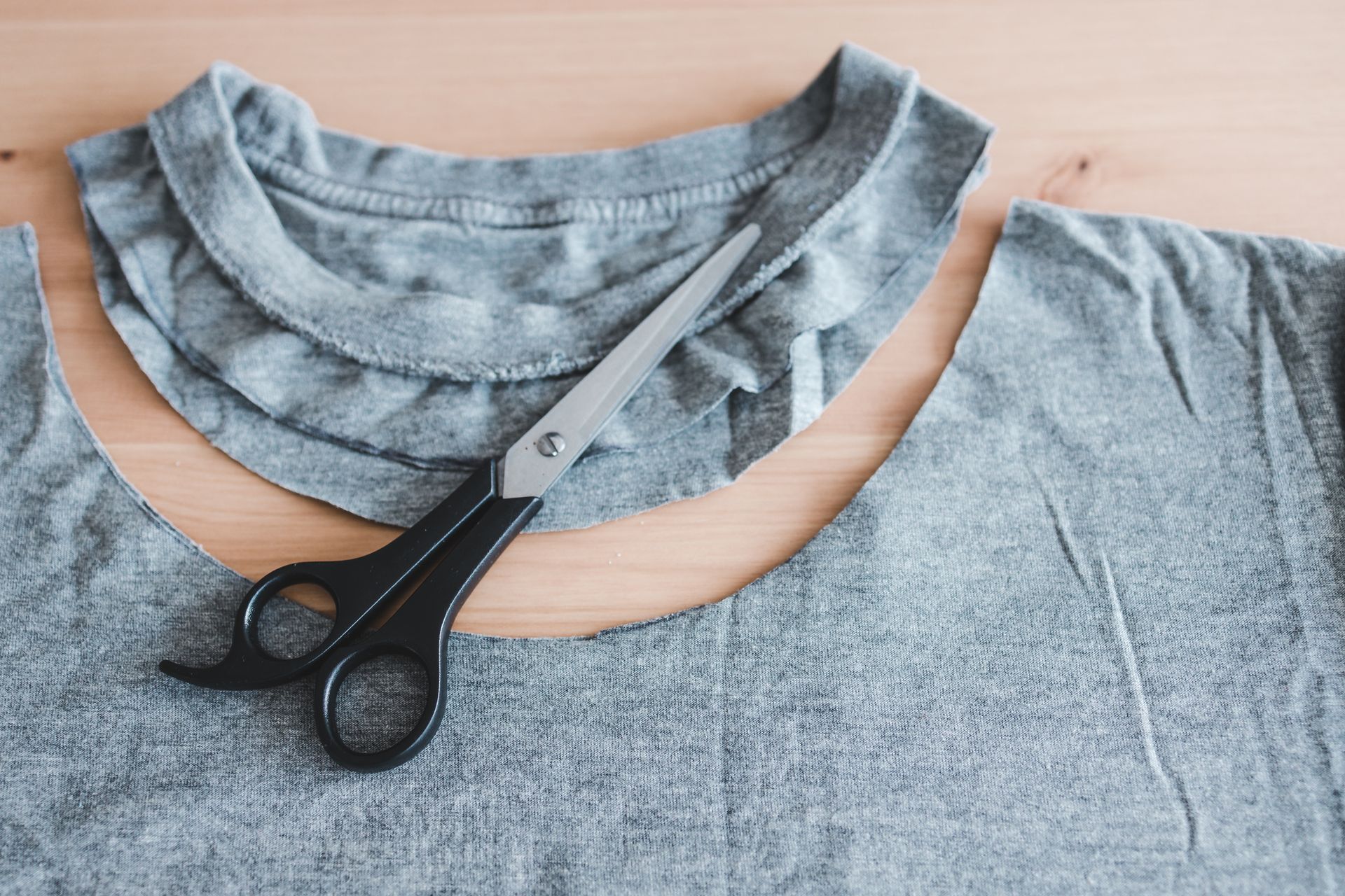 Scissors cutting the neckline of a gray T-shirt on a wooden surface