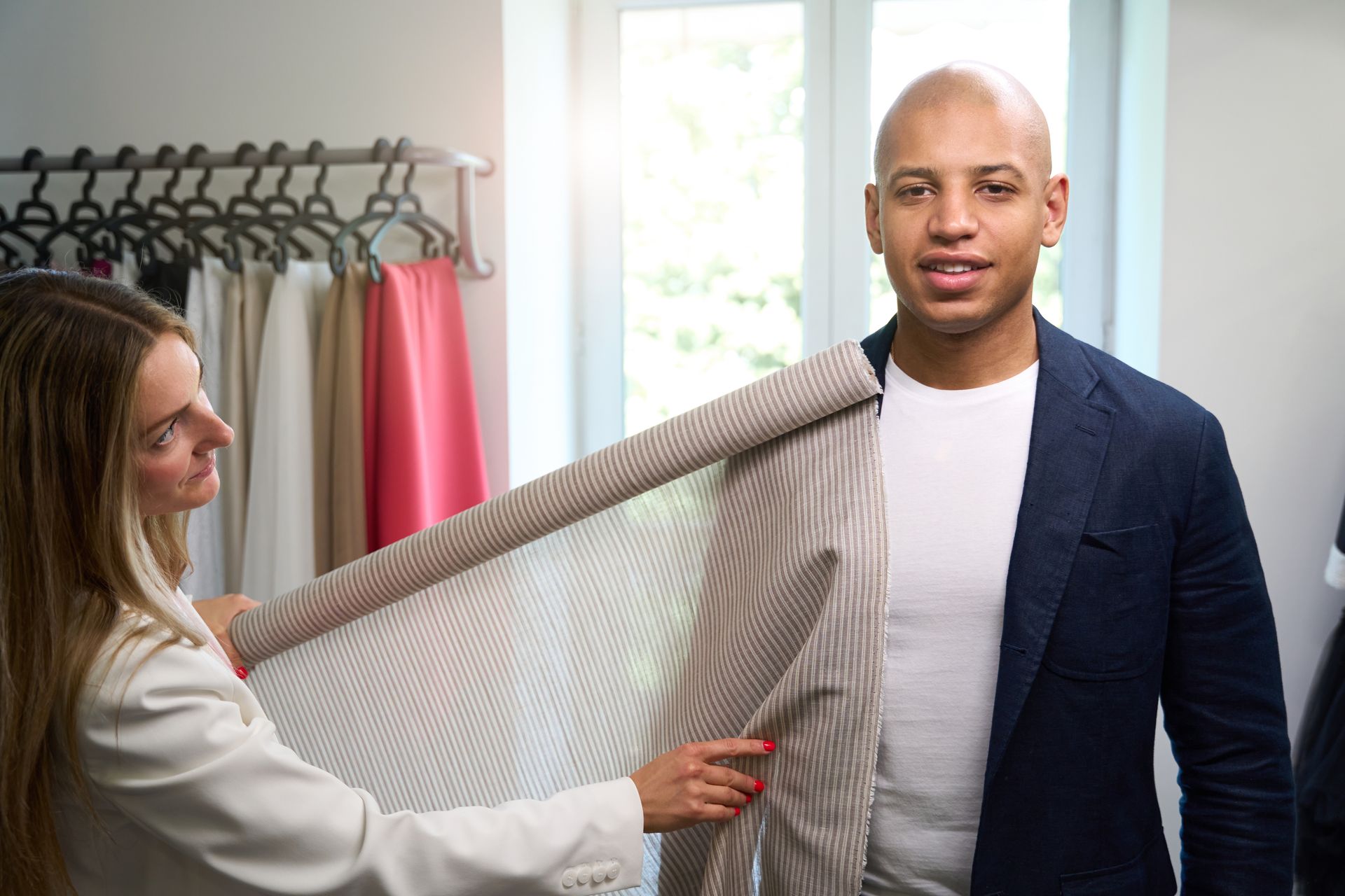 Woman in a clothing store holding up a gray fabric sample toward a man standing beside her