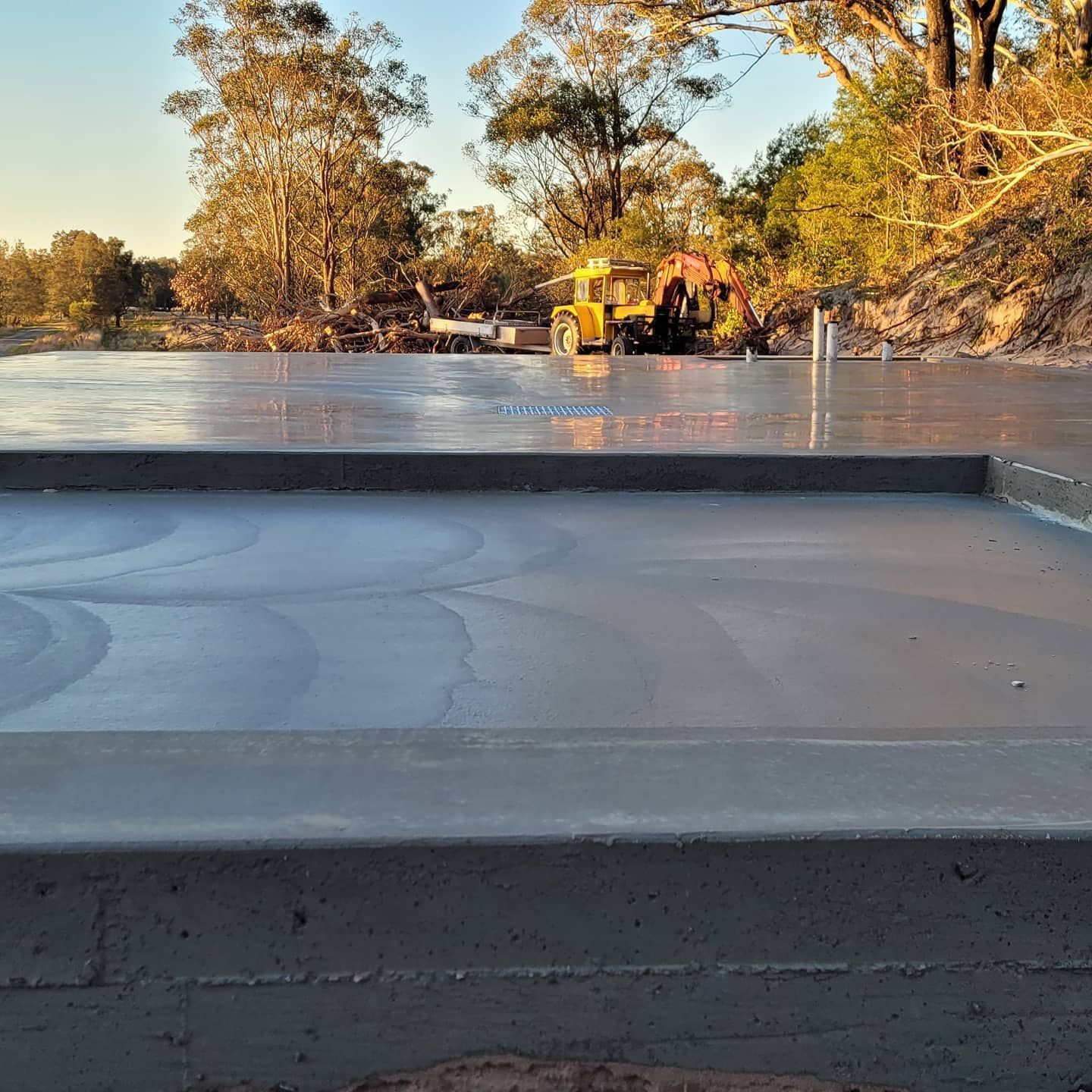 A Concrete Floor With A Yellow Tractor In The Background — Dave Smith Concrete in Mallabula, NSW