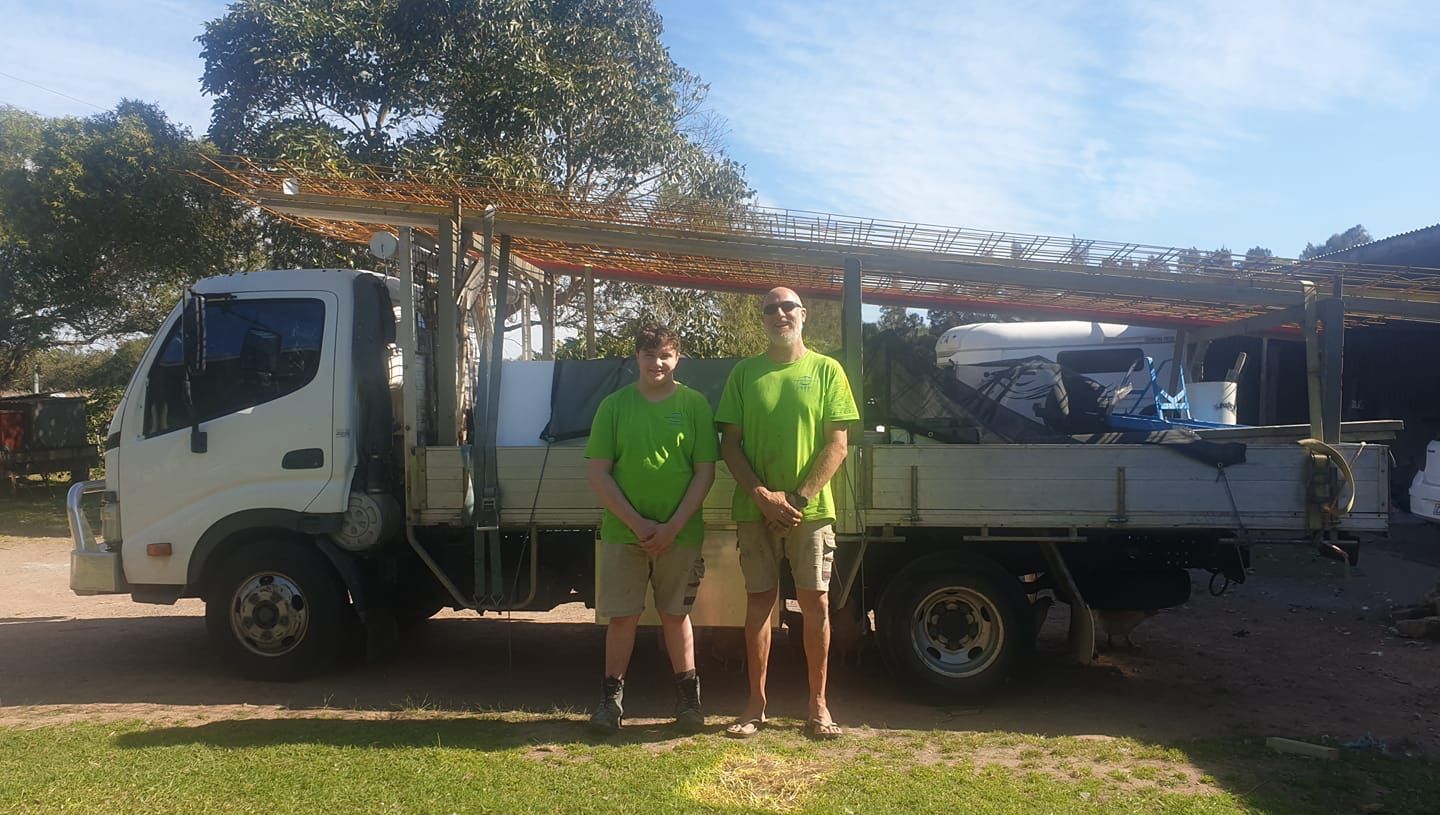Two Men In Green Shirts Are Standing In Front Of A Truck — Dave Smith Concrete in Salt Ash, NSW