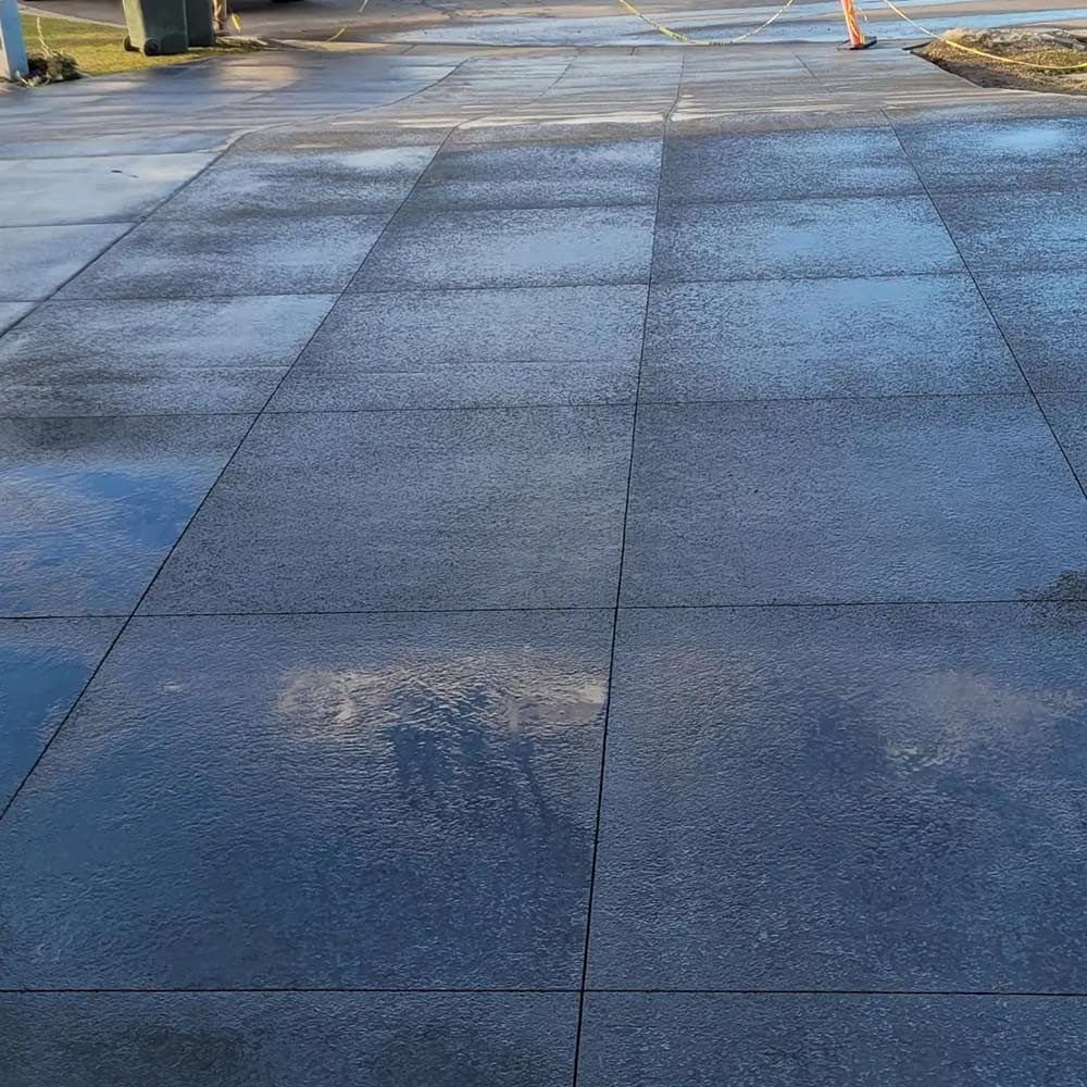 A Person is Sweeping a Concrete Driveway With a Broom — Dave Smith Concrete in Maitland, NSW
