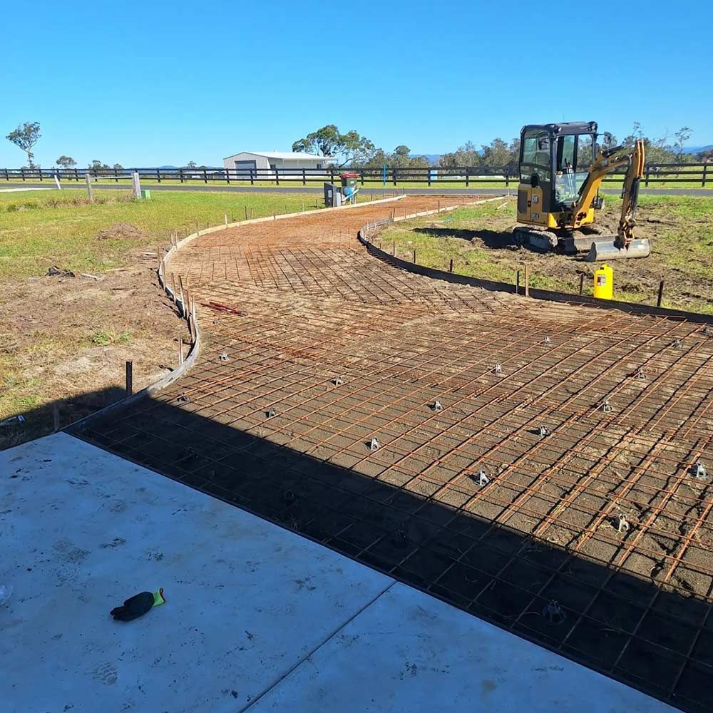 A Yellow Excavator is Working on a Dirt Road — Dave Smith Concrete in Salt Ash, NSW