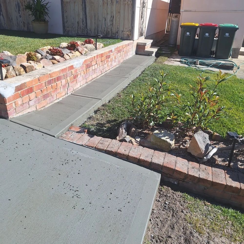A Sidewalk With A Brick Wall And Trash Cans In The Background — Dave Smith Concrete in Port Stephens, NSW