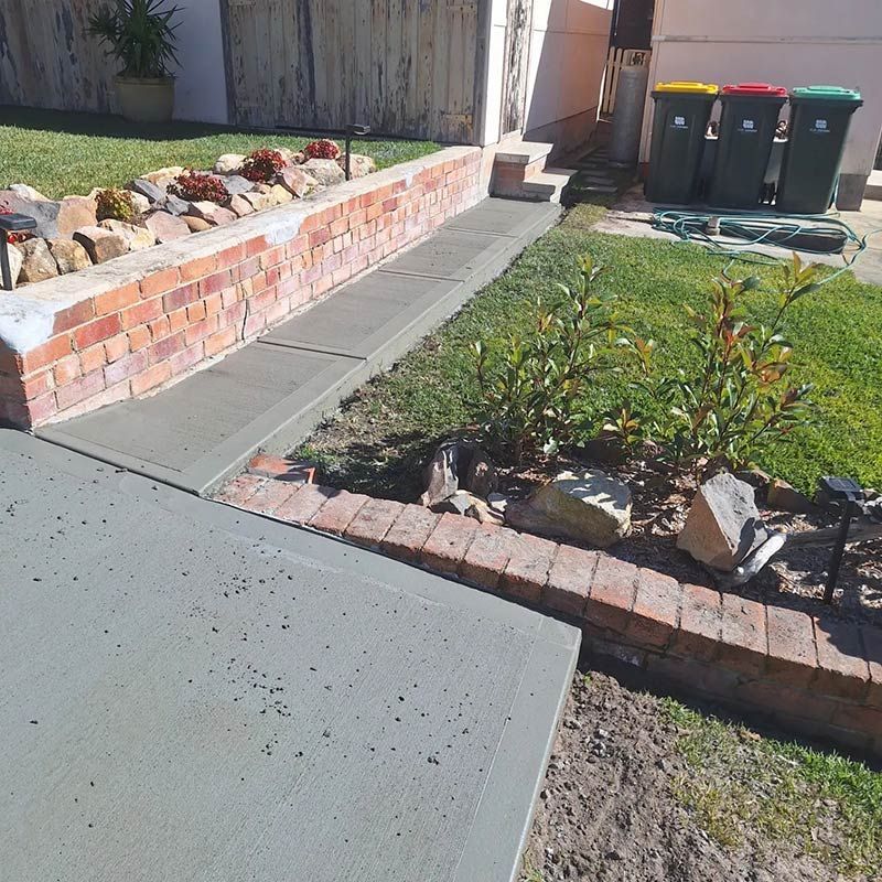 A Sidewalk With a Brick Wall and Trash Cans in the Background — Dave Smith Concrete in Salt Ash, NSW