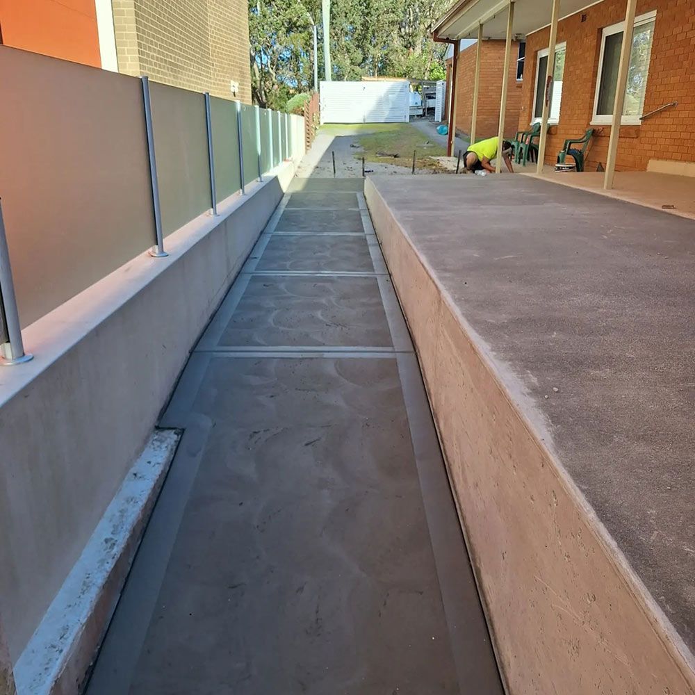 A Concrete Walkway Leading to a Brick Building — Dave Smith Concrete in Central Coast, NSW