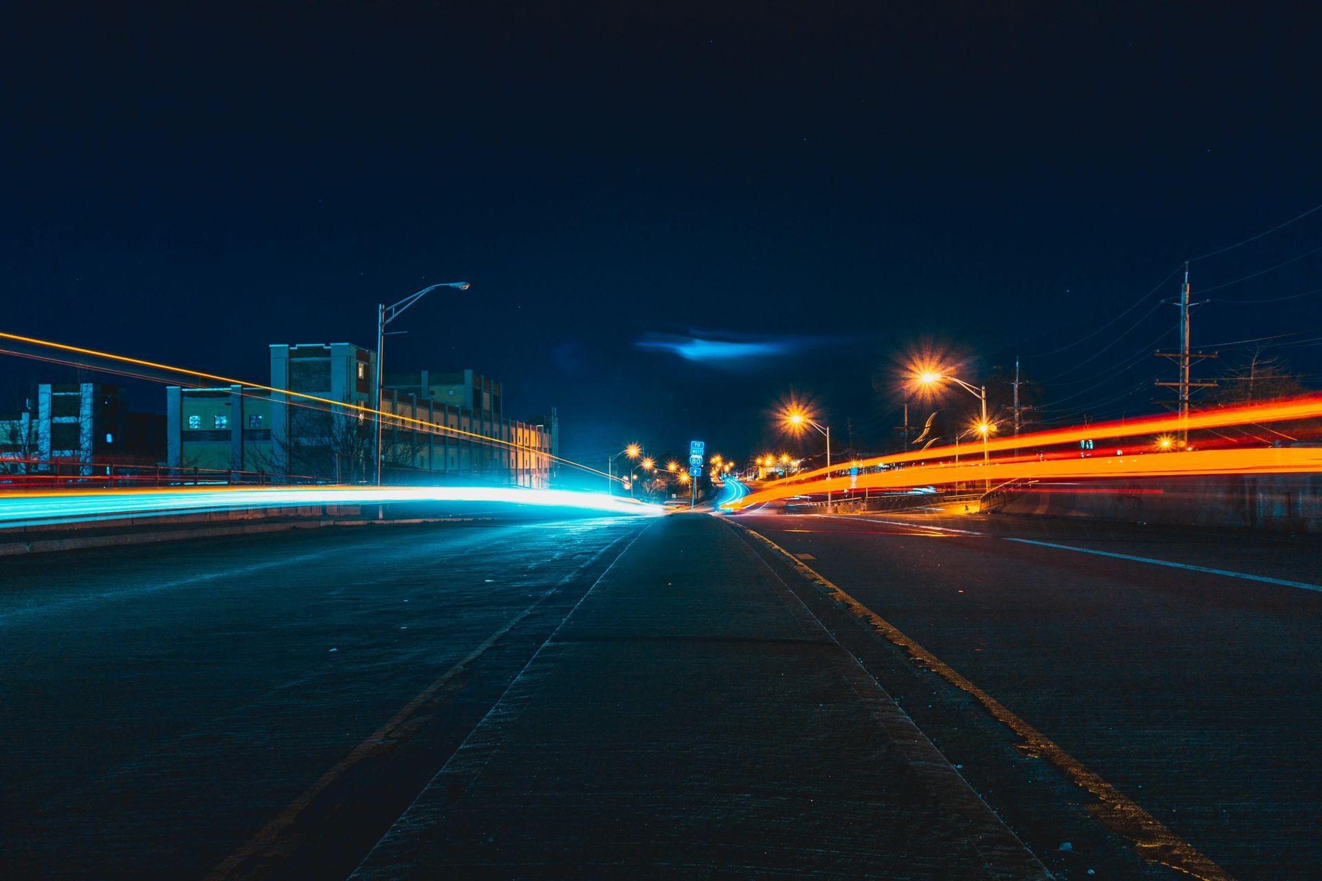 Long exposure shot of city street at night, with streaks of blue and orange light from passing vehicles.