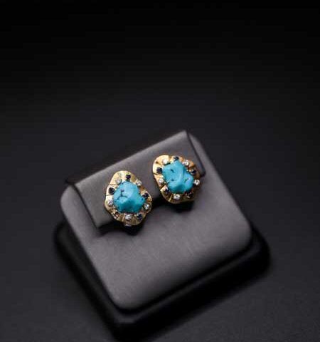 Turquoise gemstone stud earrings with gold and silver accents on a black display cushion