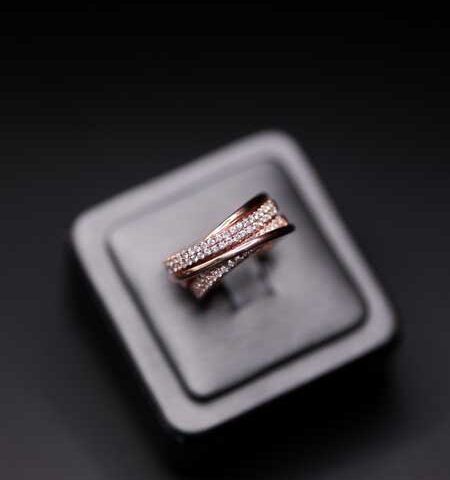 A rose gold ring with diamonds on a black display stand