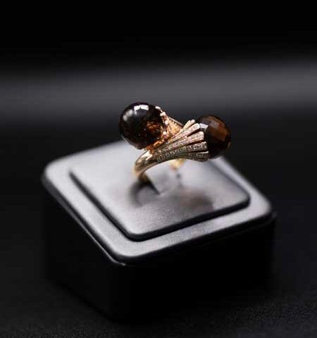 Gold ring with dark gemstone accents displayed on a black jewelry stand
