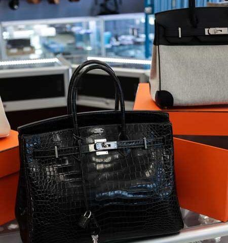 Black crocodile-textured handbag on an orange display shelf in a store, with a gray bag behind it