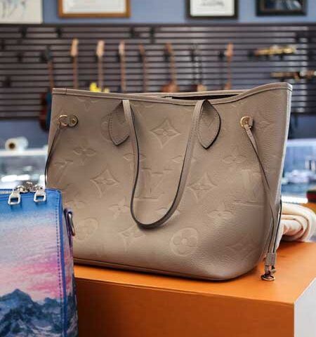 Taupe monogram tote bag on a display table with a blue gradient handbag beside it