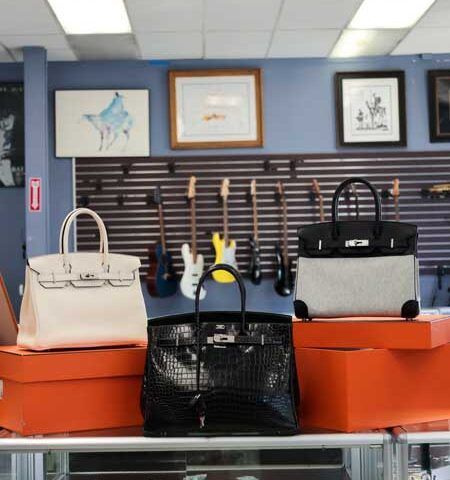 Three handbags displayed on orange boxes in a store with framed art on the wall.