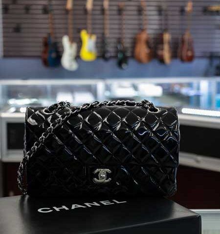 Black Chanel quilted handbag on a Chanel box in a luxury boutique, with guitars in the background