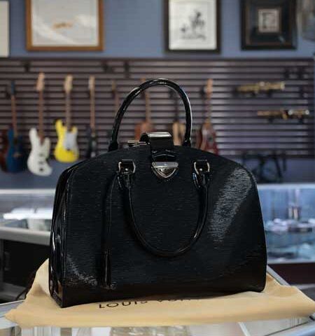 Black leather handbag on a table in a store, with guitars displayed in the background.