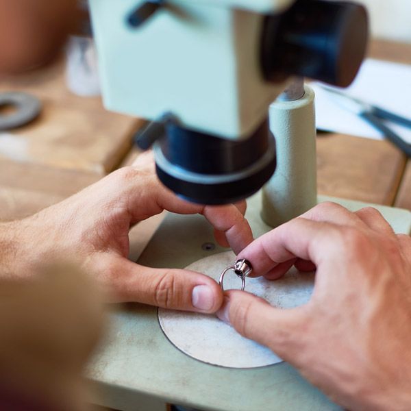 Hands adjusting a small ring under a microscope on a workbench