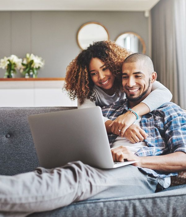 Couple smiling on a couch using a laptop in a bright living room