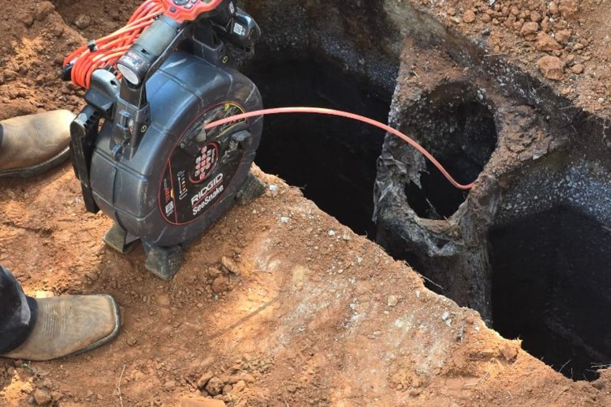 Sewer camera inspecting a dark underground tank. The camera is black and red, set on wood blocks.
