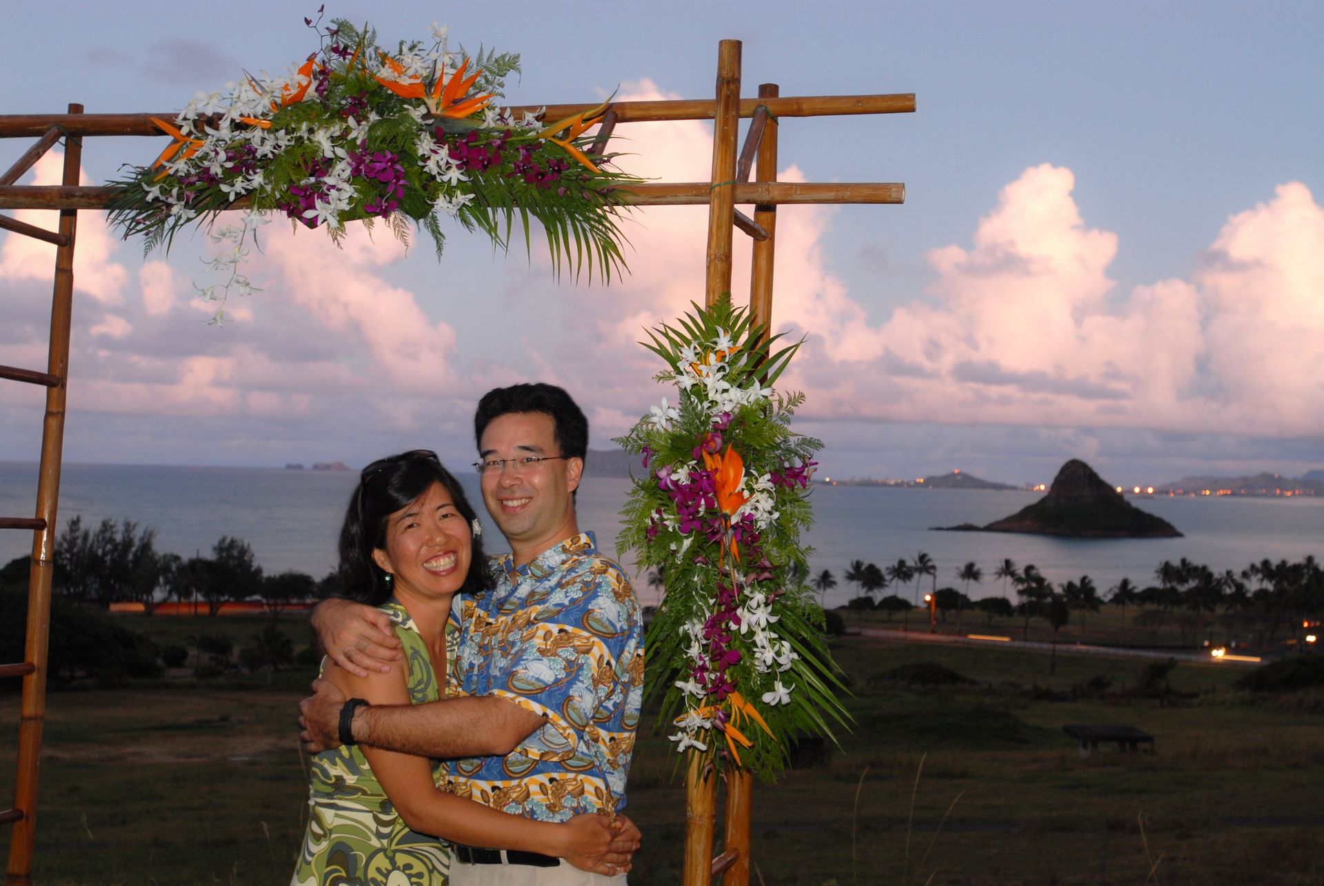 Couple embracing under floral arch at sunset overlooking the ocean