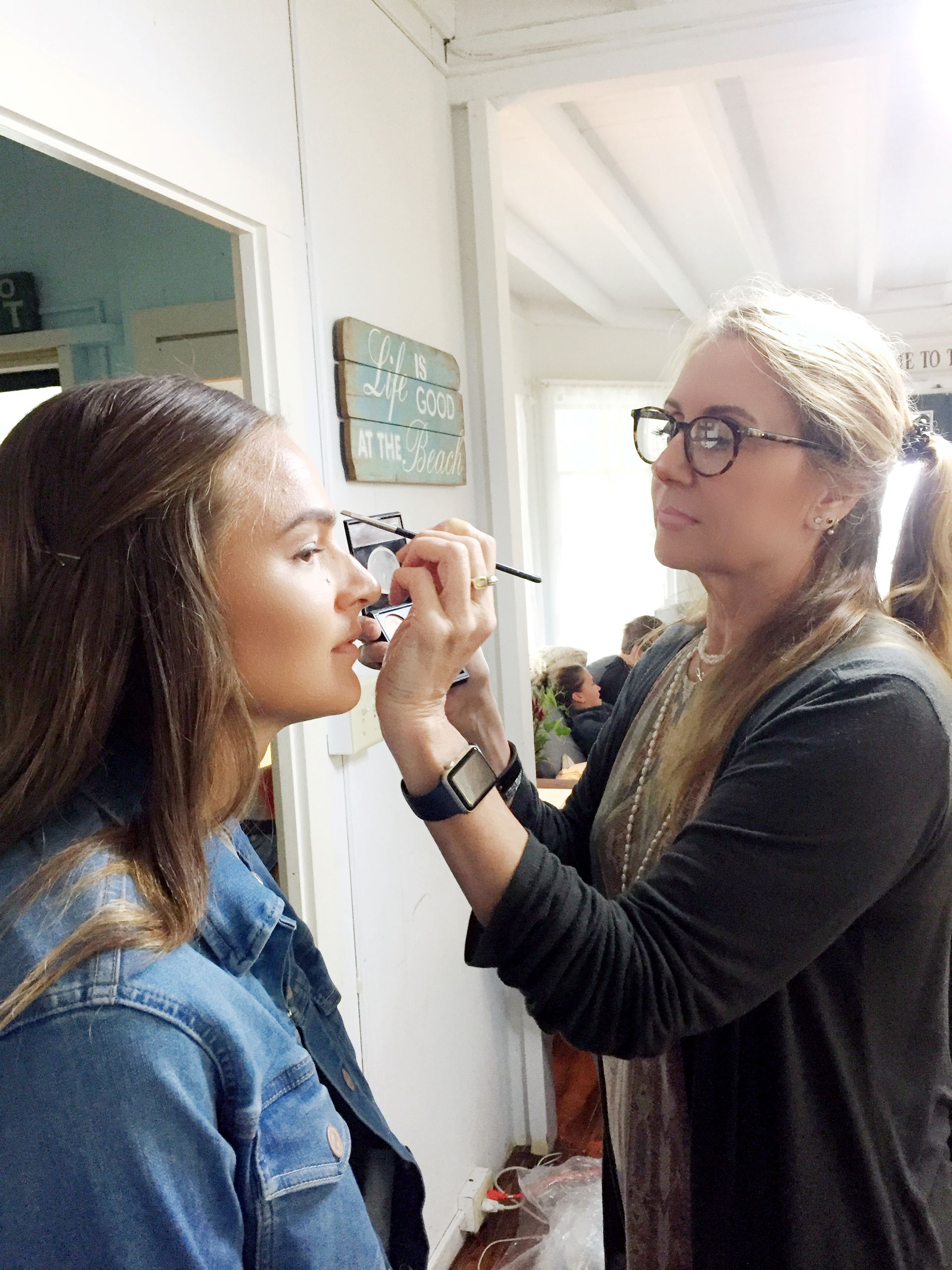 Makeup artist applying eye makeup to a seated woman in a bright room