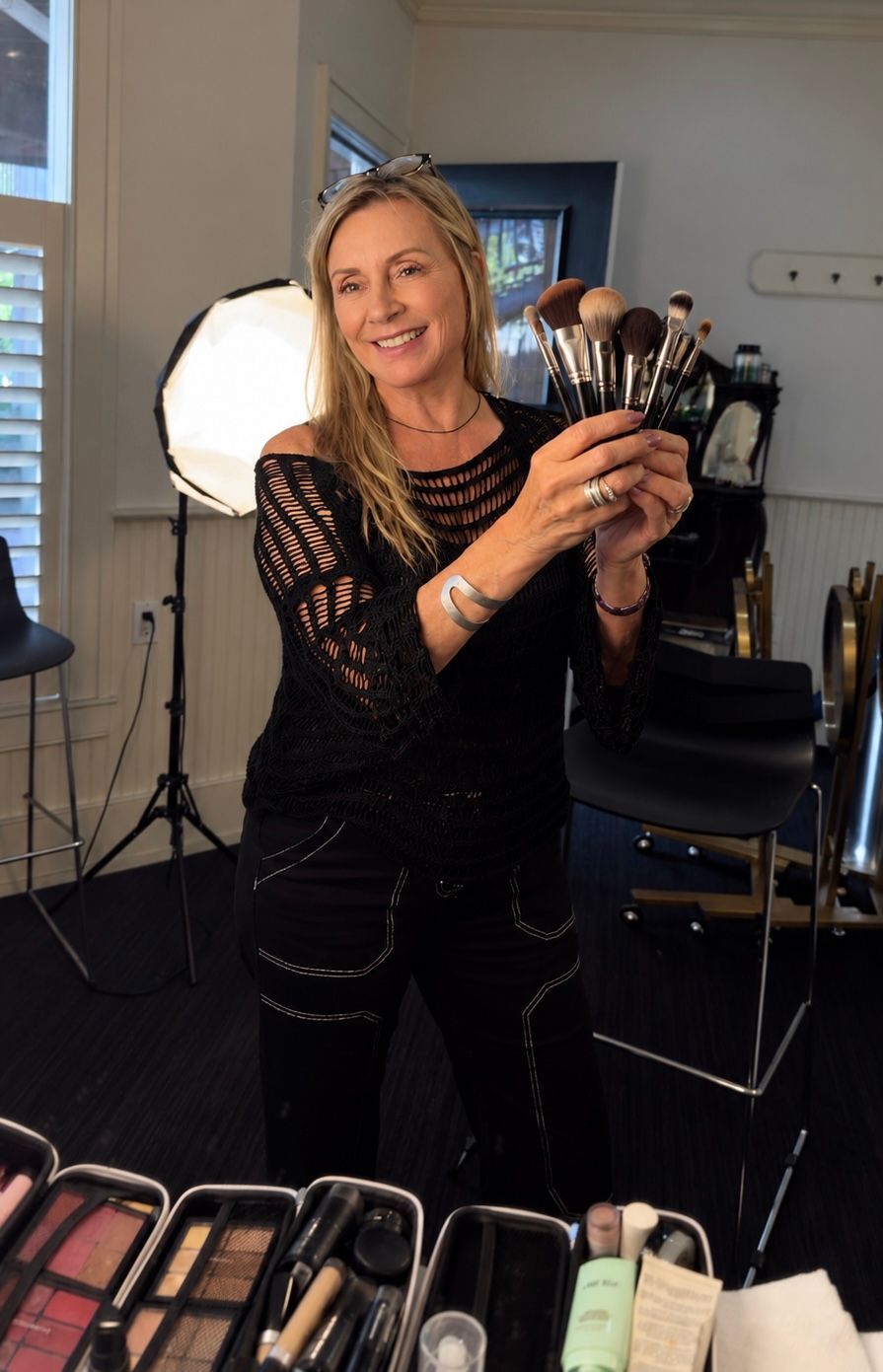 A smiling woman in a black top with skincare products on a desk in the background.