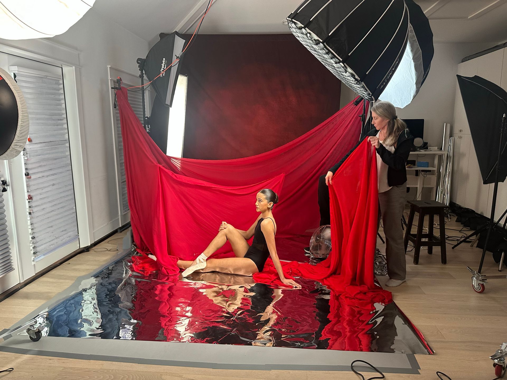Model posing on a red draped set with studio lights and reflective floor backdrop