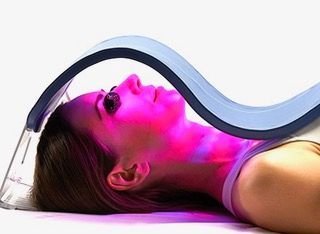 Person lying under a blue curved light therapy device with pink light on their face and neck