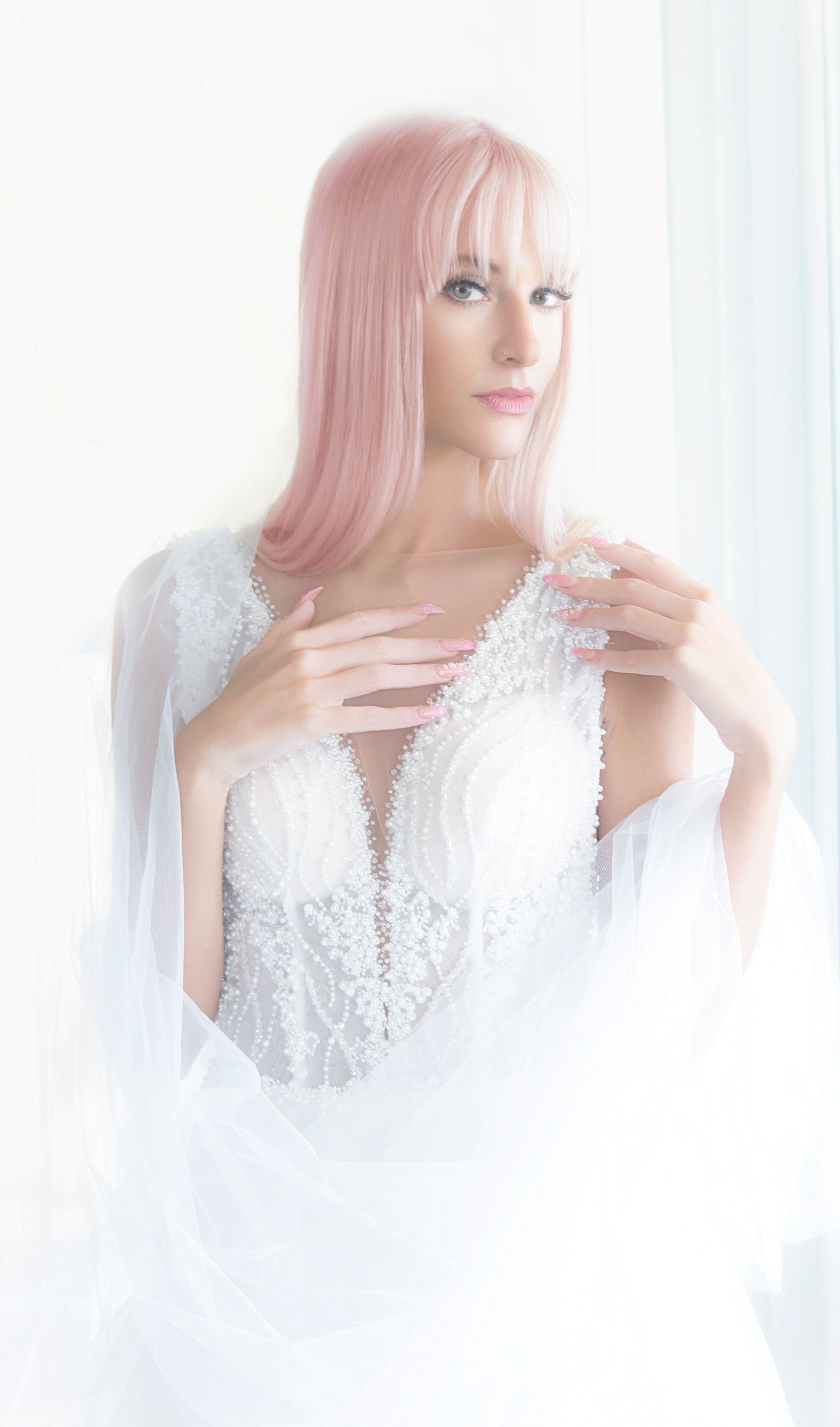 Person with pink hair in a white lace dress, standing in soft white light