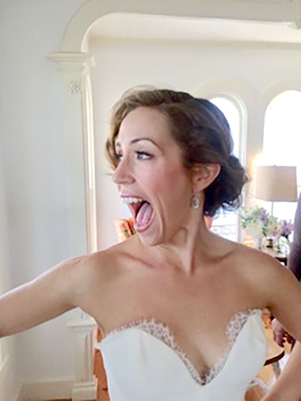 Woman in a white dress laughing with mouth open in a bright indoor setting