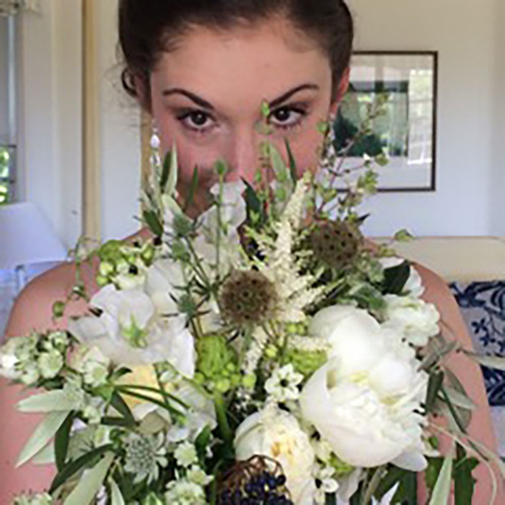Woman peering over a white flower bouquet indoors