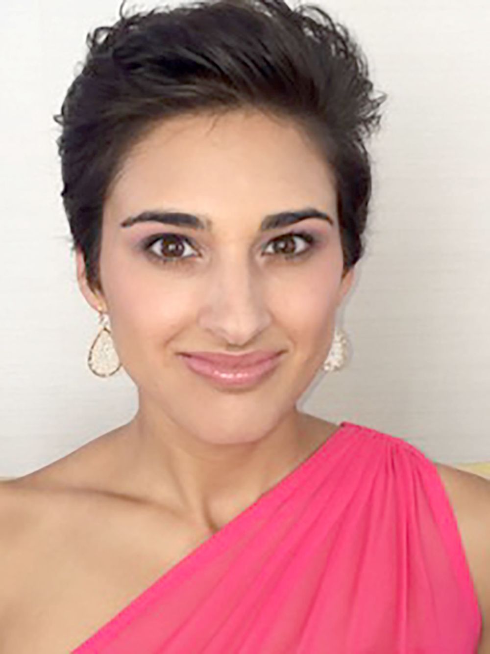 Portrait of a smiling person in a bright pink one-shoulder top and teardrop earrings on a white background