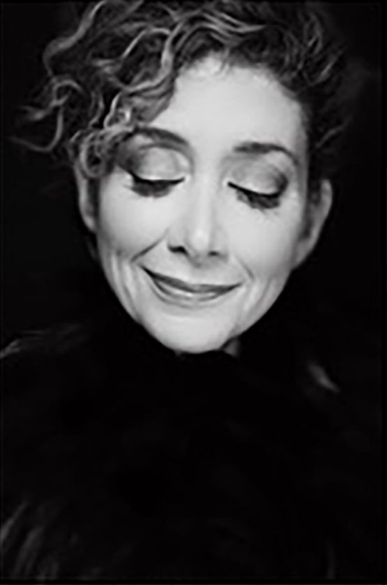 Black-and-white portrait of a person with eyes closed, smiling softly against a dark background