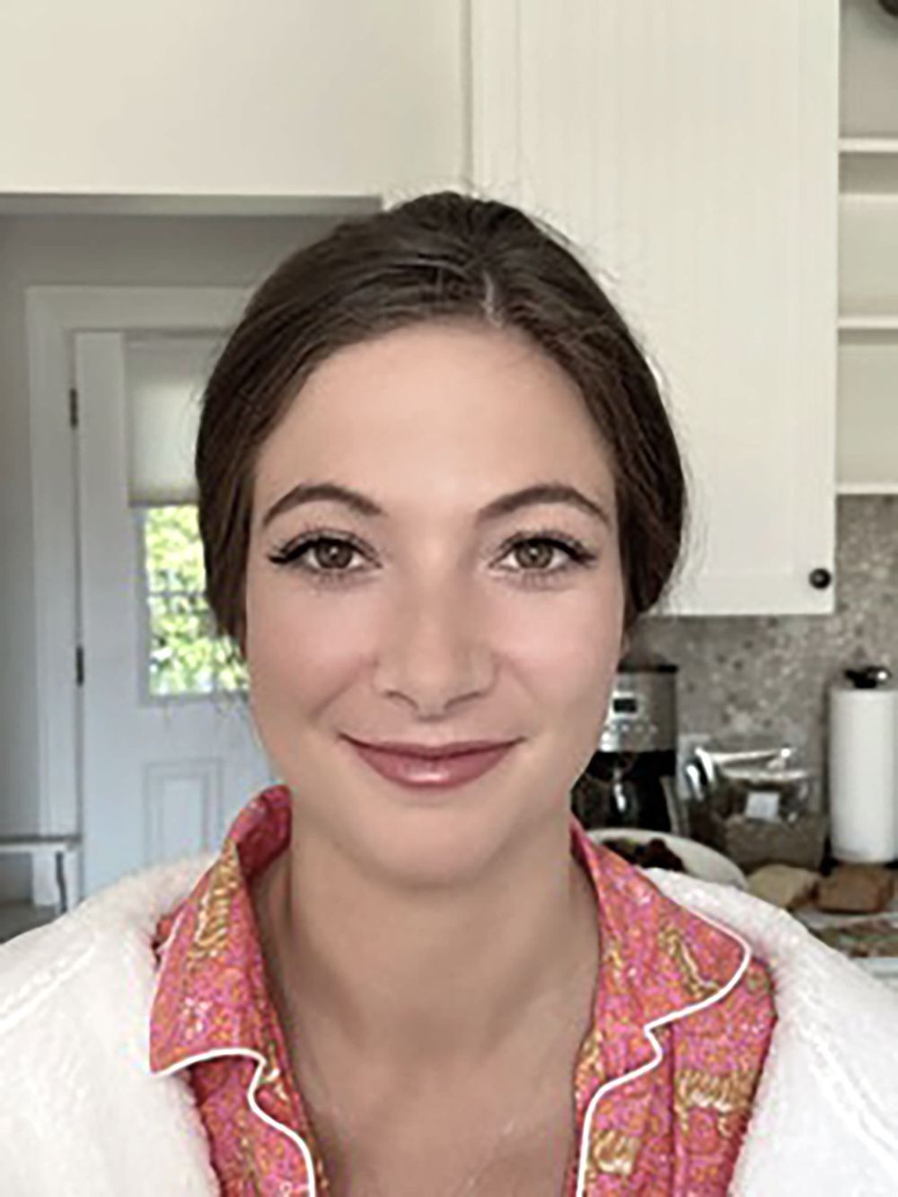 Portrait of a smiling woman in a pink shirt and white jacket in a kitchen